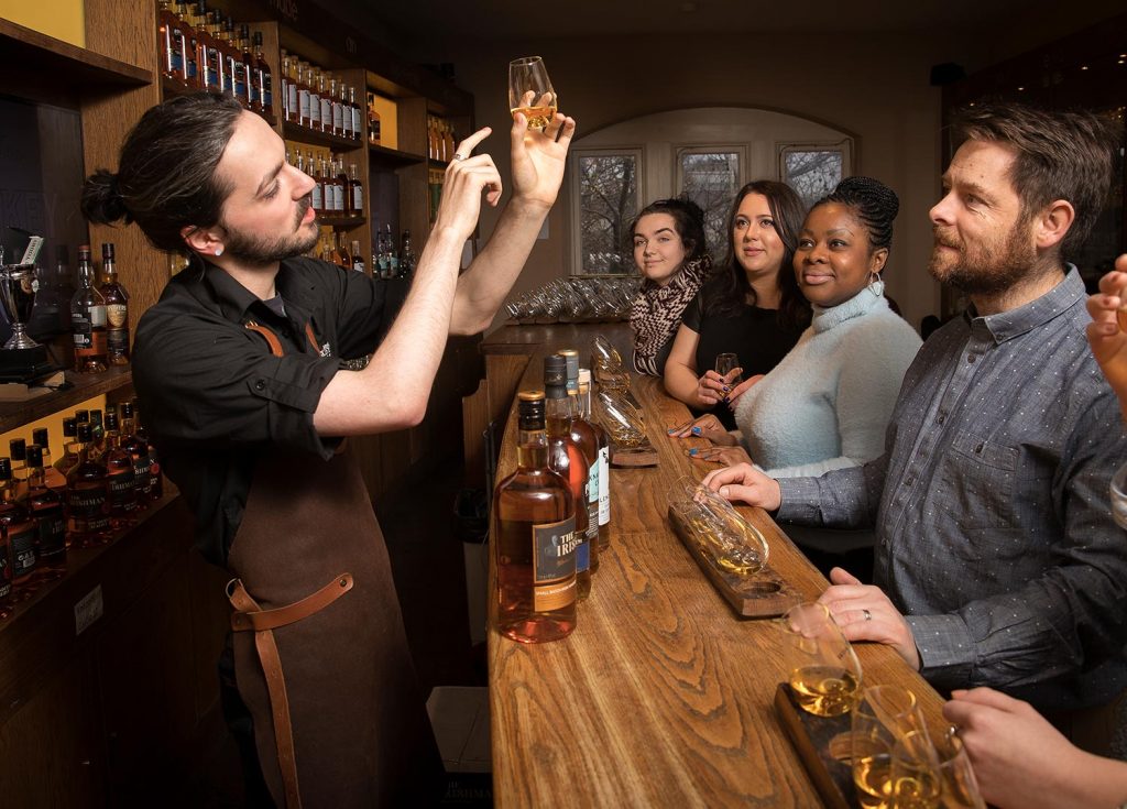barman showing whiskey in glass to customers